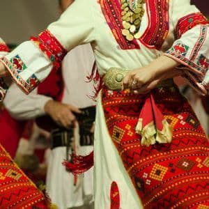 A close-up of people in traditional embroidered folk costumes holding hands while performing a folk dance.