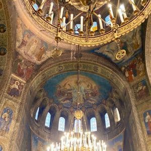 Looking up at the frescoed dome of an ornate cathedral with large golden chandeliers hanging from the ceiling.