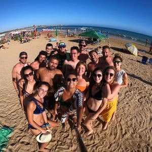 Un grupo de WeRoad se toma una selfie en una playa de arena concurrida un día soleado.