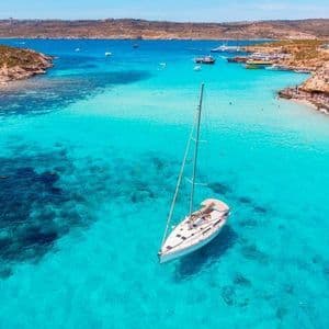 Un voilier blanc ancré dans une crique aux eaux turquoises et limpides, entouré de falaises rocheuses et d'autres bateaux.