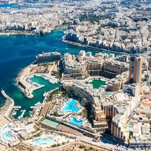 Une vue aérienne d'une ville côtière dense avec des bâtiments modernes entourant une marina remplie de bateaux par une journée ensoleillée.