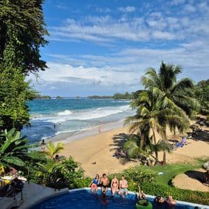 Un voyage de groupe WeRoad, détente en piscine avec vue sur une plage tropicale, ses palmiers et l'océan sous un ciel légèrement nuageux.