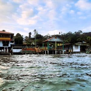 Vue depuis l'eau de maisons colorées sur pilotis sur un rivage luxuriant, l'une affichant un panneau 'Bienvenidos'.