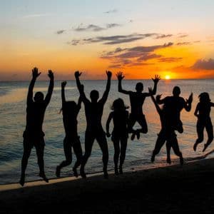 Siluetas de un viaje en grupo de WeRoad saltando en una playa de arena durante una puesta de sol sobre el océano.