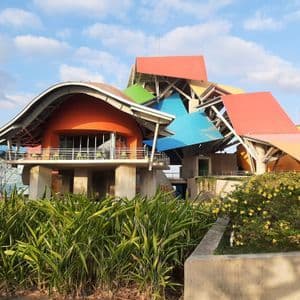 Un bâtiment coloré à l'architecture moderne et abstraite, doté de toits superposés et multicolores, est vu depuis un jardin.