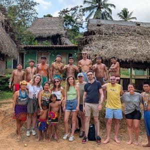 Des voyageurs de WeRoad posent pour une photo avec des membres d'une communauté indigène devant des cabanes traditionnelles au toit de chaume.