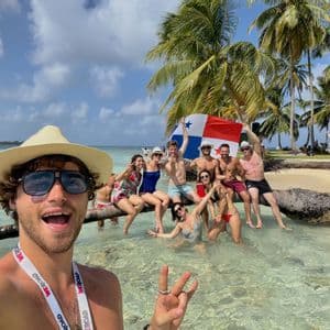 Un groupe WeRoad prend un selfie sur une plage tropicale, posant dans l'eau claire et tenant un drapeau panaméen.