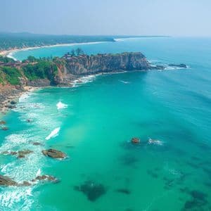 Una vista aerea di una costa tropicale con scogliere verdi lussureggianti, spiagge sabbiose e acqua turchese vibrante sotto un cielo sereno.