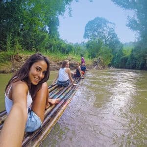 Una mujer se toma una selfie sonriente con su grupo de WeRoad en una balsa de bambú flotando por un río rodeado de jungla.