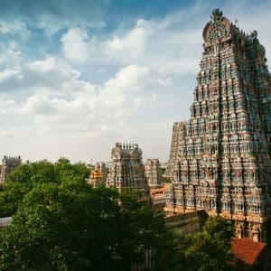 Prunkvolle und farbenprächtige Hindu-Tempeltürme erheben sich über grünen Baumwipfeln unter einem teilweise bewölkten blauen Himmel.