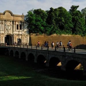 Un gruppo WeRoad attraversa a piedi e in bicicletta un ponte ad arco in pietra che porta a un'antica porta fortificata.