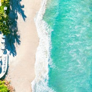 Una vista aerea dall'alto di acqua turchese e onde bianche che incontrano una spiaggia sabbiosa fiancheggiata da palme.