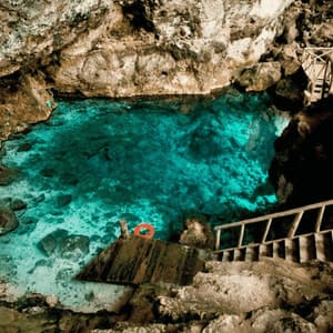 Una scala di legno conduce a un piccolo pontile su un cenote con acqua limpida e turchese all'interno di una grotta rocciosa.