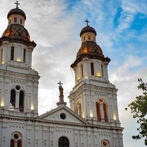 Le due torri bianche di una cattedrale con cupole piastrellate sono illuminate contro un cielo parzialmente nuvoloso.