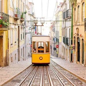 A yellow funicular tram on a track ascends a steep, narrow cobblestone street lined with colorful historic buildings.