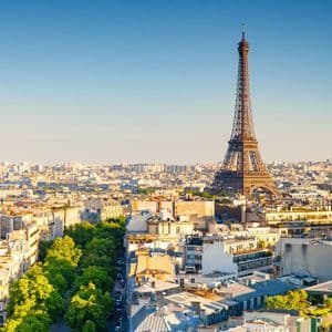 An aerial view of the Paris cityscape with the Eiffel Tower rising above the rooftops under a clear blue sky.