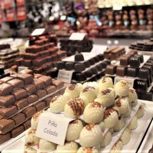 Pyramids of milk, dark, and white chocolates displayed on white trays in a confectionary shop.