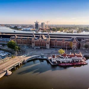 Aerial view of a historic red-brick building and modern city skyline along a wide canal under a clear blue sky.