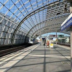 A train waits at a platform in a modern station under a large, arched glass and steel ceiling.