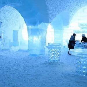 L'interno di un ice bar con soffitti ad arco, pilastri e tavoli scolpiti nel ghiaccio, con due persone al bancone.