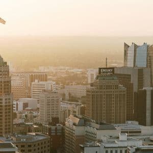 An American flag flies atop a skyscraper in a dense city skyline bathed in the hazy golden light of sunset.