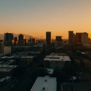 A city skyline with tall buildings and mountains in the background, illuminated by the warm glow of a sunset.