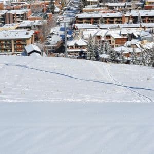 A high-angle view of a snow-covered mountain town from a snowy slope with tracks in the foreground.