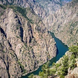 A high-angle view of a deep, rocky canyon with a dark blue river winding through the bottom and sparse green trees on the cliffs.