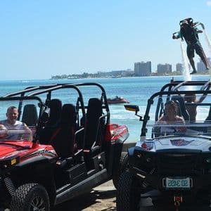 A WeRoad group trip with two off-road buggies at the beach, while a person on a flyboard levitates over the water.