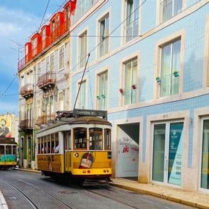 Un classico tram giallo percorre i binari lungo una strada cittadina, accanto a edifici colorati con facciate piastrellate.