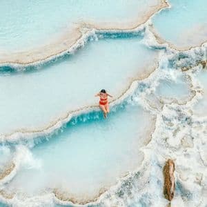 Vista aerea di una donna in bikini rosso che si rilassa in una serie di piscine termali terrazzate azzurre lattiginose.