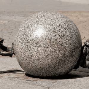 Due piccole statue di gnomi in bronzo spingono una grande sfera di granito da lati opposti su una pavimentazione in pietra.