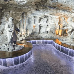 Sculture di roccia salina raffiguranti minatori sono esposte all'interno di una caverna sotterranea con una passerella illuminata e moderna.