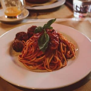 A plate of spaghetti and meatballs with tomato sauce, garnished with a basil leaf, on a restaurant table.