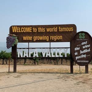A large wooden welcome sign for Napa Valley, a wine growing region, stands in front of a vineyard with rows of grapevines.
