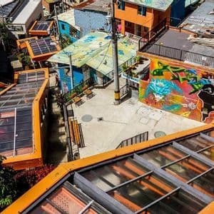 An overhead view of outdoor escalators with orange roofs running through a colorful neighborhood with graffiti on a wall.