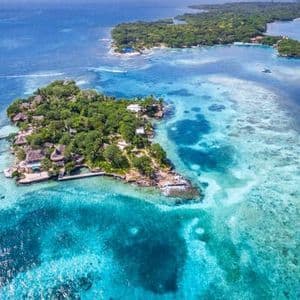 An aerial view of lush tropical islands with small resorts surrounded by clear, shallow turquoise waters.