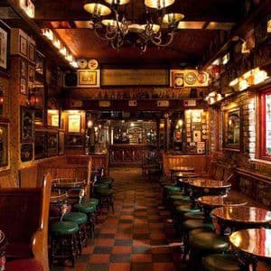 L'interno accogliente di un pub classico con divanetti in legno scuro, tavoli rotondi, sgabelli verdi e un pavimento a scacchi.