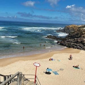 Una vista dall'alto di una spiaggia sabbiosa in una caletta rocciosa, con persone che nuotano nel mare e prendono il sole sulla sabbia.