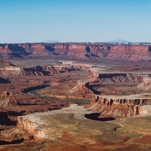 An expansive view of a deep red rock canyon with a river snaking through the canyon floor under a clear sky.