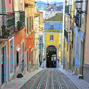 Una vista in discesa su una ripida strada acciottolata con binari del tram, fiancheggiata da edifici colorati e con una funicolare in fondo.
