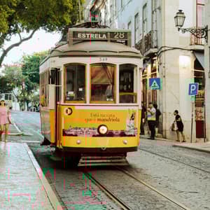 Un tram d'epoca giallo e bianco percorre i binari su una stretta strada di ciottoli accanto a vecchi edifici cittadini.