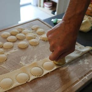 A person's hand using a cutter to make fresh ravioli on a wooden board dusted with flour.