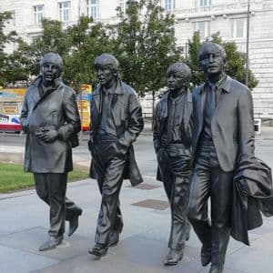 Life-size bronze statues of the four members of The Beatles walking along a city pavement in front of a building.