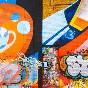 A brick wall covered in vibrant and colorful graffiti, with a door in the center that is plastered with stickers.