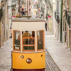 Una funicolare gialla con passeggeri a bordo sale lungo una ripida e stretta strada di ciottoli fiancheggiata da edifici.