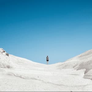 Un viandante solitario con uno zaino si staglia su una duna bianca contro un cielo blu intenso.