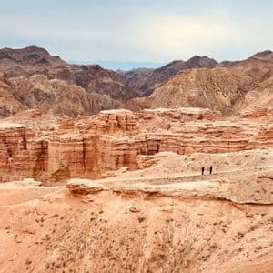 Zwei Personen einer WeRoad-Gruppenreise stehen auf einem Bergrücken und blicken auf einen weiten Canyon aus roten Felsformationen.