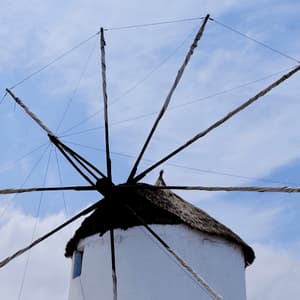 Un tradizionale mulino a vento bianco con tetto di paglia e vele ammainate si erge contro un cielo azzurro con nuvole bianche.