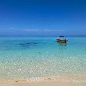A yellow motorboat anchored in calm, turquoise ocean water near a sandy beach under a clear blue sky.